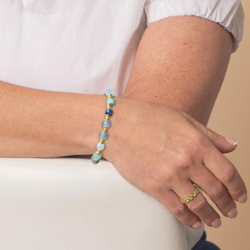 Woman modeling the Selene beaded bracelet in gold with soft blue and aqua beads, designed for interchangeable medical IDs.