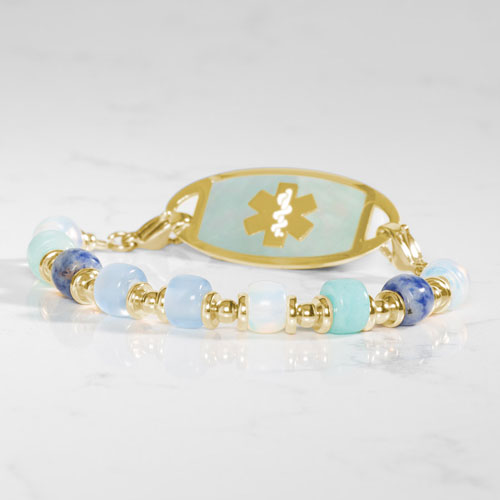 Gold-tone medical ID bracelet featuring a mother-of-pearl alert tag, Star of Life symbol, and coordinating Selene bead strand.