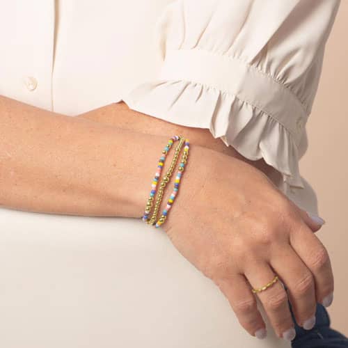 Model wearing a gold tone beaded bracelet with colorful seed beads on wrist.
