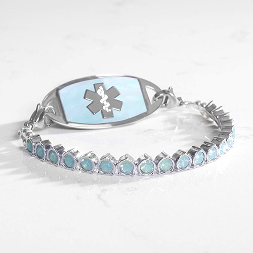 Silver-tone medical ID bracelet featuring a full strand of shimmering blue opal crystals and an inlay-style ID tag with a soft blue opalescent face and silver medical emblem.