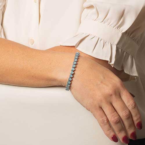 Woman wearing a silver toned bracelet featuring iridescent blue opal stones.