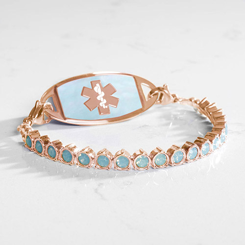 Rose gold medical alert bracelet with light blue opal stones and iridescent opal inlay tag, displayed on marble surface.