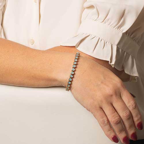 Woman wearing a silver toned bracelet featuring iridescent blue opal stones.