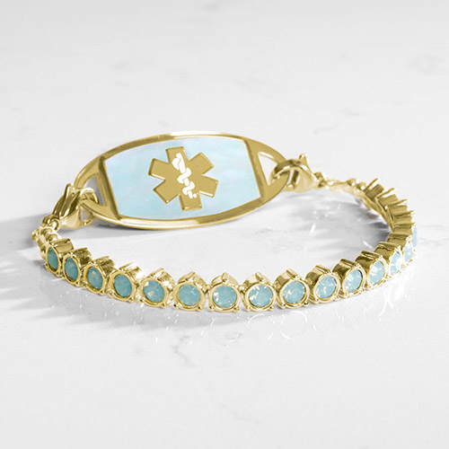 Gold medical ID bracelet with blue opal crystals and a matching gold and opal ID tag, displayed on white marble
