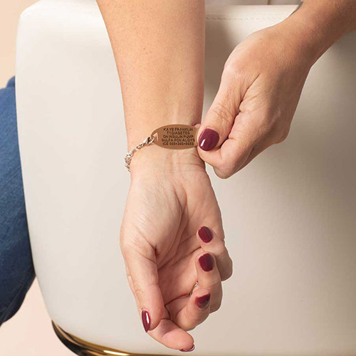 Close-up of a woman adjusting a rose gold medical ID bracelet engraved with emergency information on her wrist.