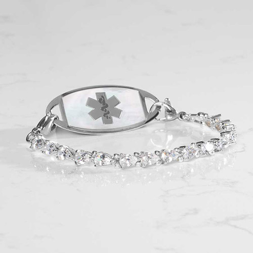 Rhodium-plated women's medical ID bracelet with stretch design, featuring pear-cut cubic zirconia and a mother-of-pearl ID tag with medical symbol, displayed on white marble.