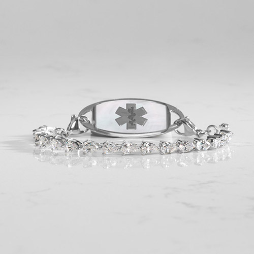 Rhodium-plated women's medical ID bracelet with stretch design, featuring pear-cut cubic zirconia and a mother-of-pearl ID tag with medical symbol, displayed on white marble.