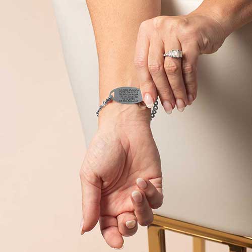 Woman’s wrist turned to display the back of a silver medical ID bracelet engraved with emergency medical information, attached with a silver chain.