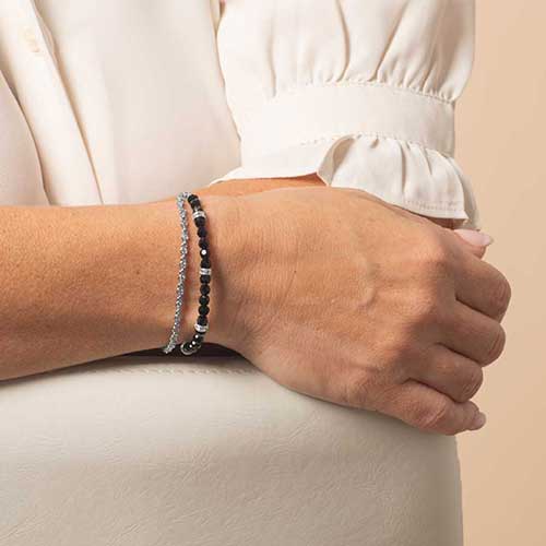 Close-up of a woman's wrist wearing a layered silver medical ID bracelet with two strands—one with black faceted beads and silver rondelles, and the other a delicate silver crystal chain.