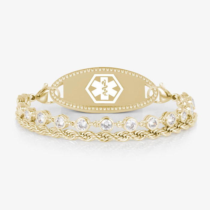 A gold-tone medical ID bracelet featuring two chains—one rope-style and one with bezel-set clear crystals—attached to a polished oval medical ID tag with a white Star of Life emblem. Displayed on a white background.