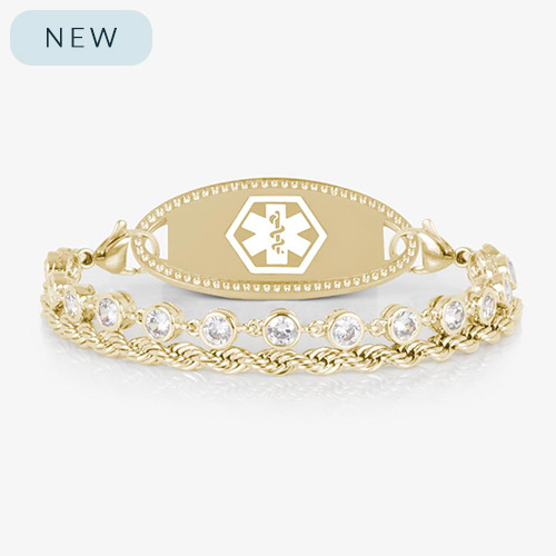 A gold-tone medical ID bracelet featuring two chains—one rope-style and one with bezel-set clear crystals—attached to a polished oval medical ID tag with a white Star of Life emblem. Displayed on a white background.