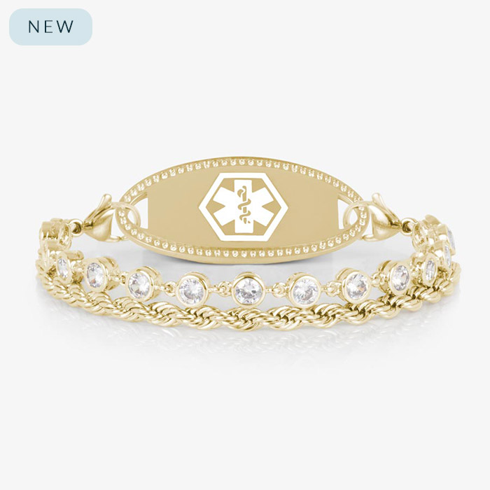 A gold-tone medical ID bracelet featuring two chains—one rope-style and one with bezel-set clear crystals—attached to a polished oval medical ID tag with a white Star of Life emblem. Displayed on a white background.