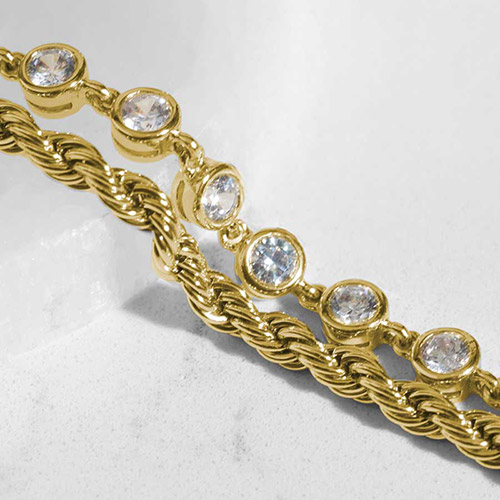 Close-up of two gold-tone chains: one a twisted rope chain, the other a CZ tennis-style strand with bezel-set round crystals.