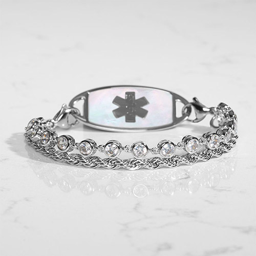 Silver medical ID bracelet displayed on a white marble surface, showing the iridescent mother-of-pearl inlay on the back of the medical ID tag with a dark engraved caduceus symbol.