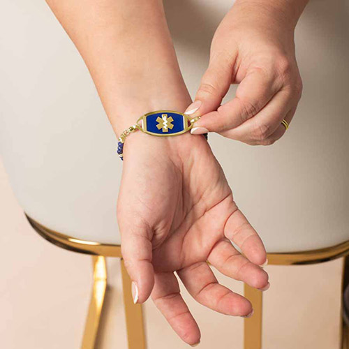 Woman showing off the front of a gold and navy medical ID bracelet featuring a medical alert symbol, paired with beaded strands for a fashionable yet functional accessory.