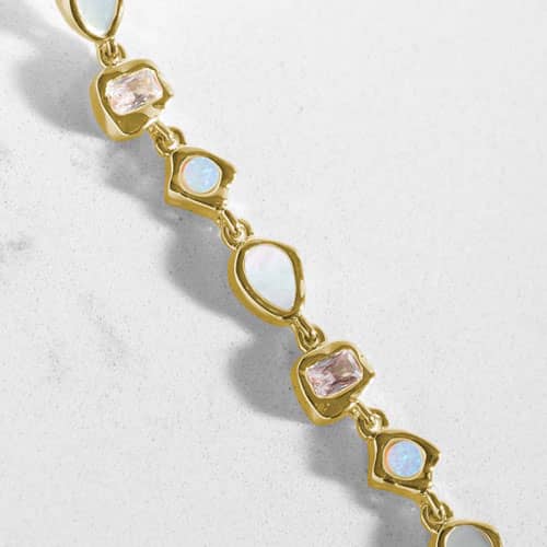 Close-up of alternating pear, oval, round, and rectangular opalescent and light pink stones in geometric gold-tone settings.