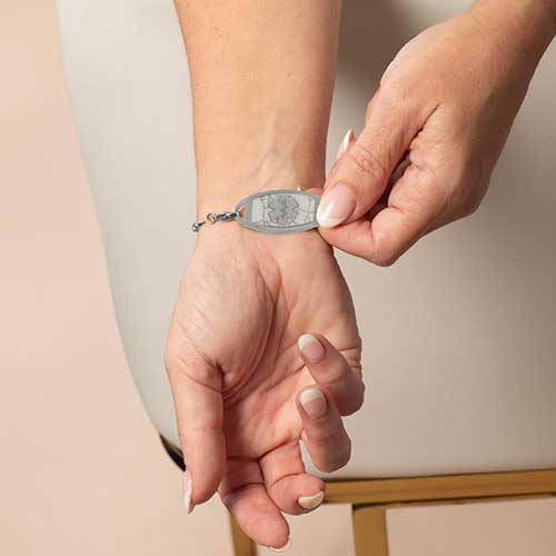 Woman showing stainless steel medical ID tag with silver medical caduceus symbol.