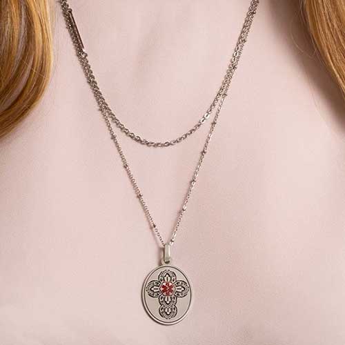 Woman in blush pink shirt wearing medical alert necklace with cross and red medical symbol