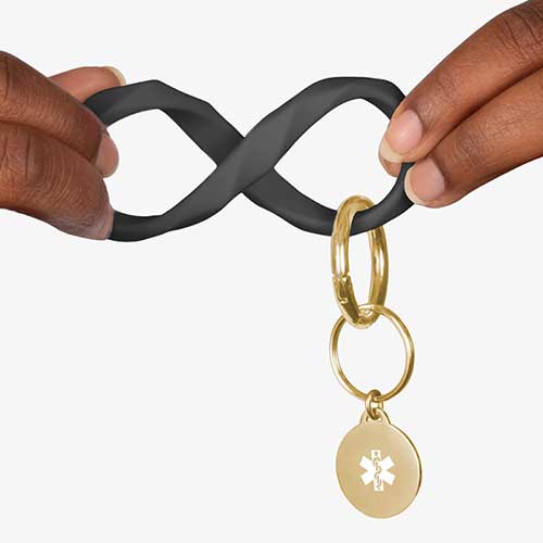 Woman twisting the black faceted silicone key ring wristlet with gold tone medical alert charm.