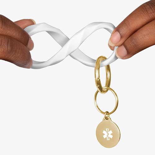 Woman twisting the white faceted silicone key ring wristlet with gold tone medical alert charm.
