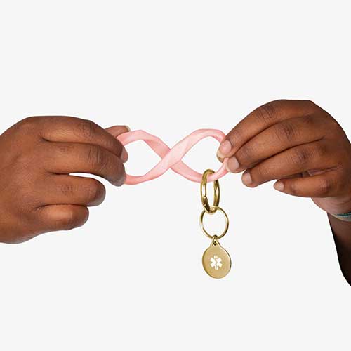 Woman twisting the soft pink faceted silicone key ring wristlet with gold tone medical alert charm.